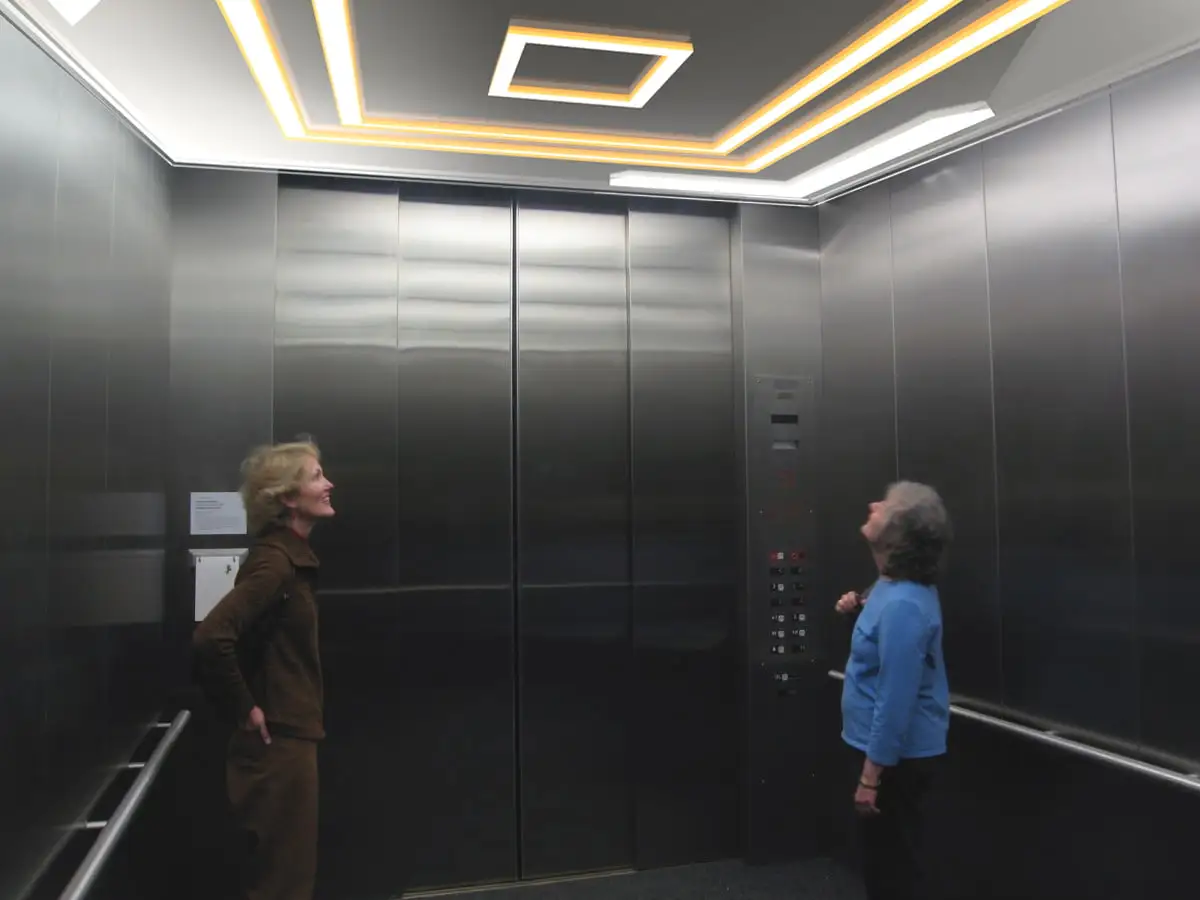 Elevator Cab Lighting Ideas illustrated with two women standing in a well lit elevator - Elevator Cab Lighting Ideas: Enhancing Ambiance and Functionality - Vorlane
